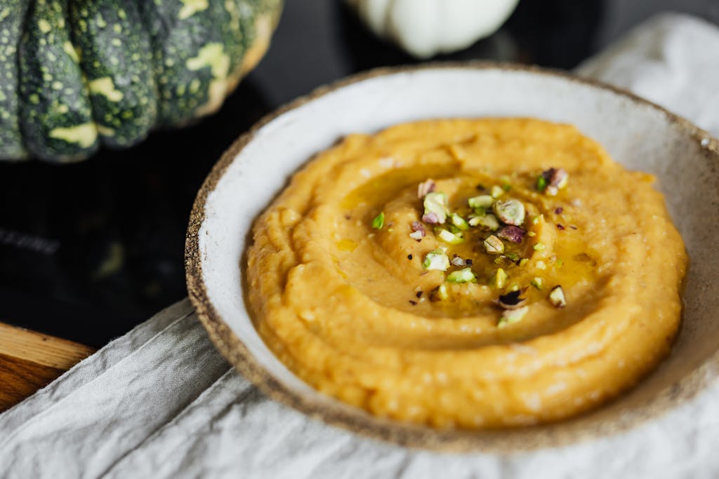 Close-up of creamy pumpkin hummus topped with pistachios in a rustic bowl.