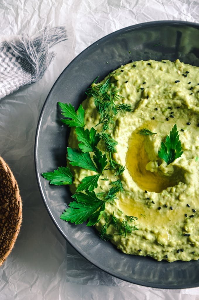 Close-up of homemade hummus garnished with fresh dill and parsley in a gray bowl.