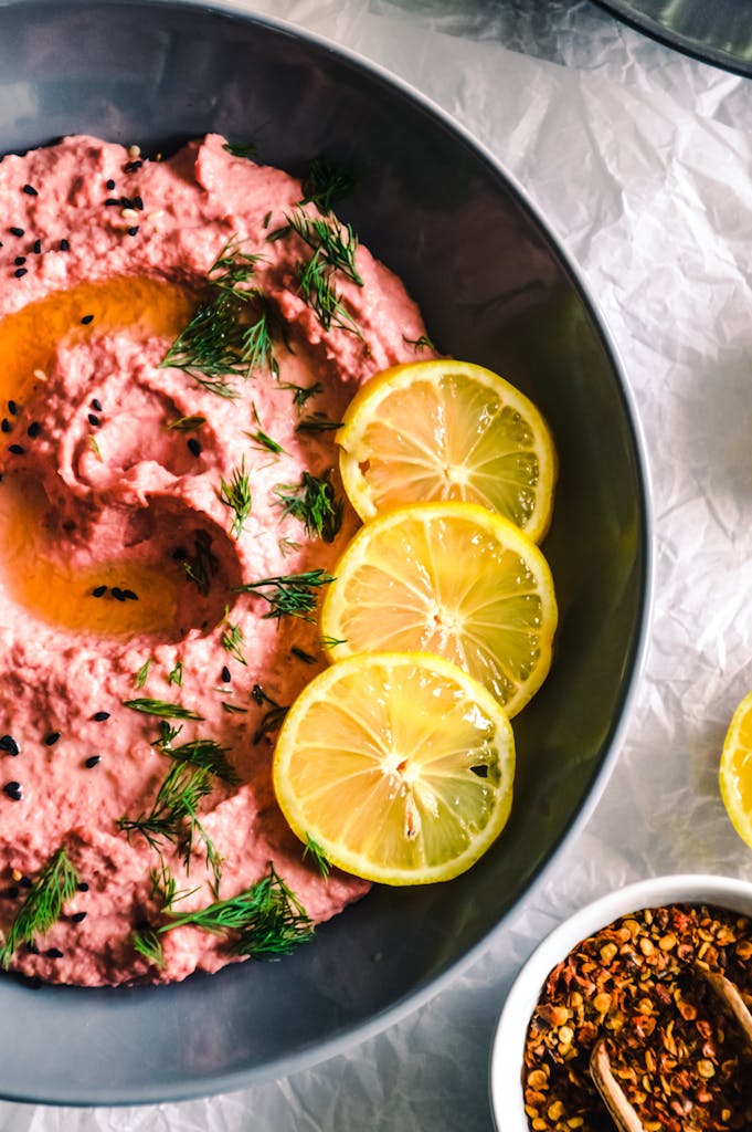 Colorful red beet hummus garnished with lemon slices and dill in a bowl.