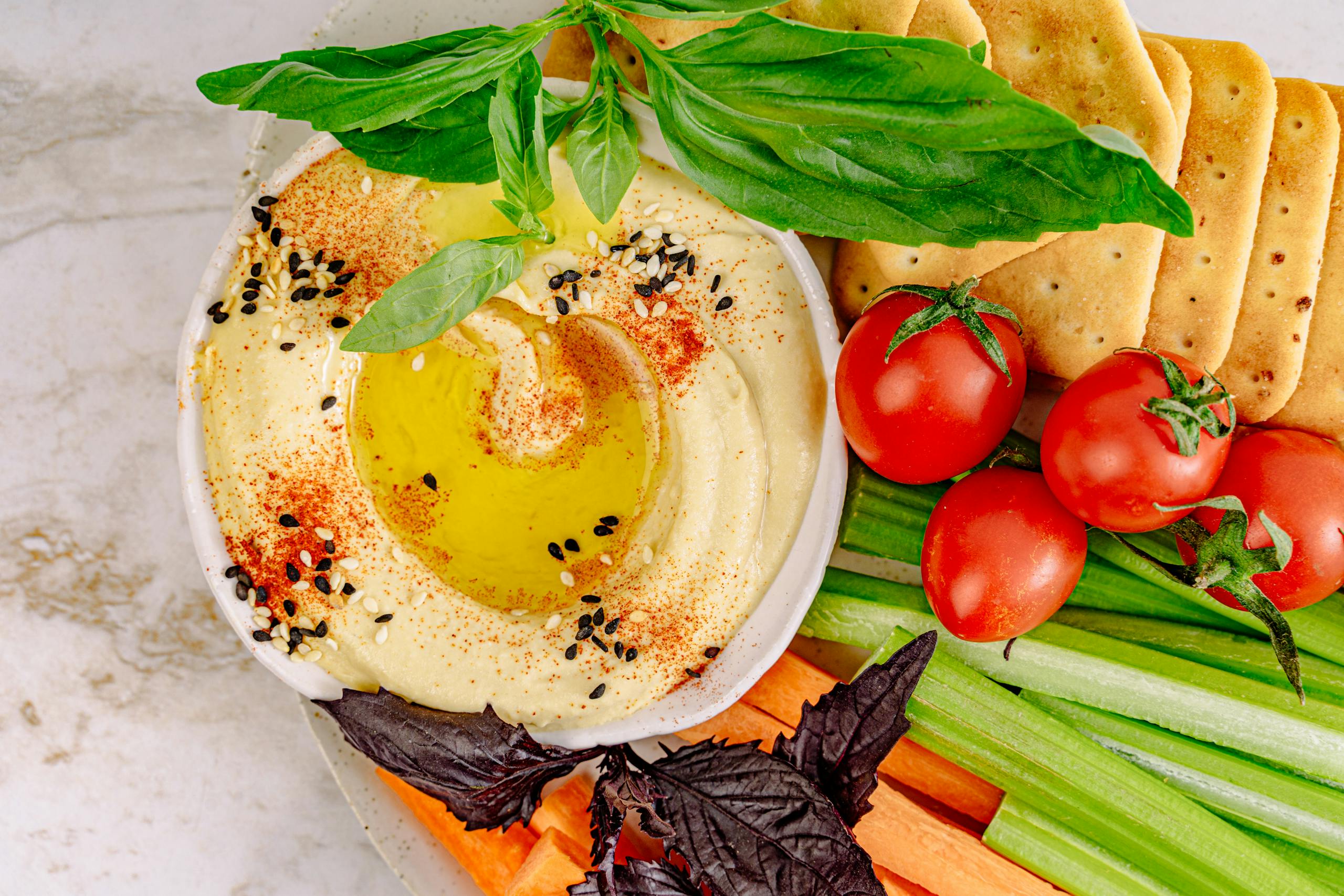 Receta de Humus Casero Plant Based - Top view of hummus with vegetables and crackers, perfect for healthy snacking.