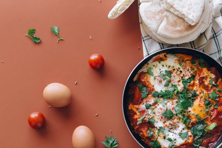 A flavorful pan of shakshuka with eggs and herbs, accompanied by pita bread.