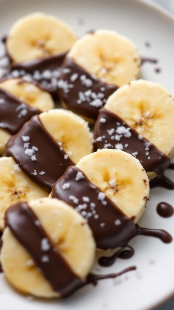 Sliced bananas dipped in dark chocolate with a sprinkle of salt on a plate.