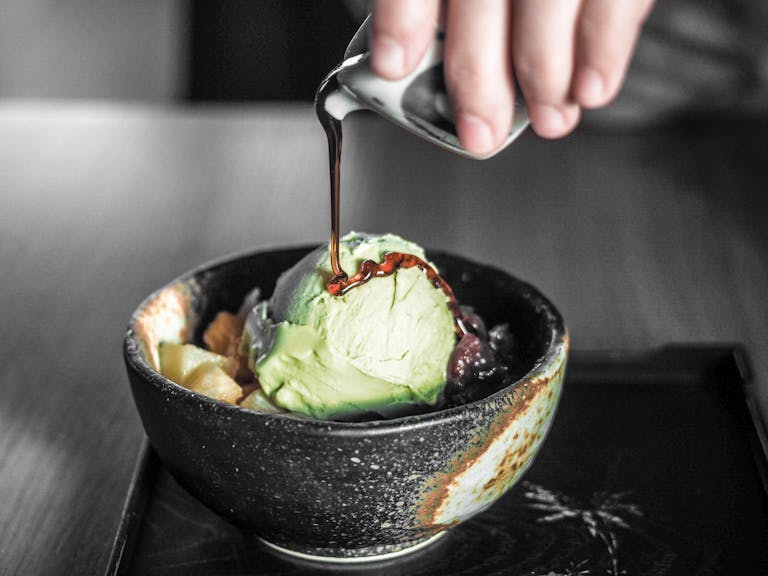 Matcha ice cream being drizzled with rich chocolate in a ceramic bowl.