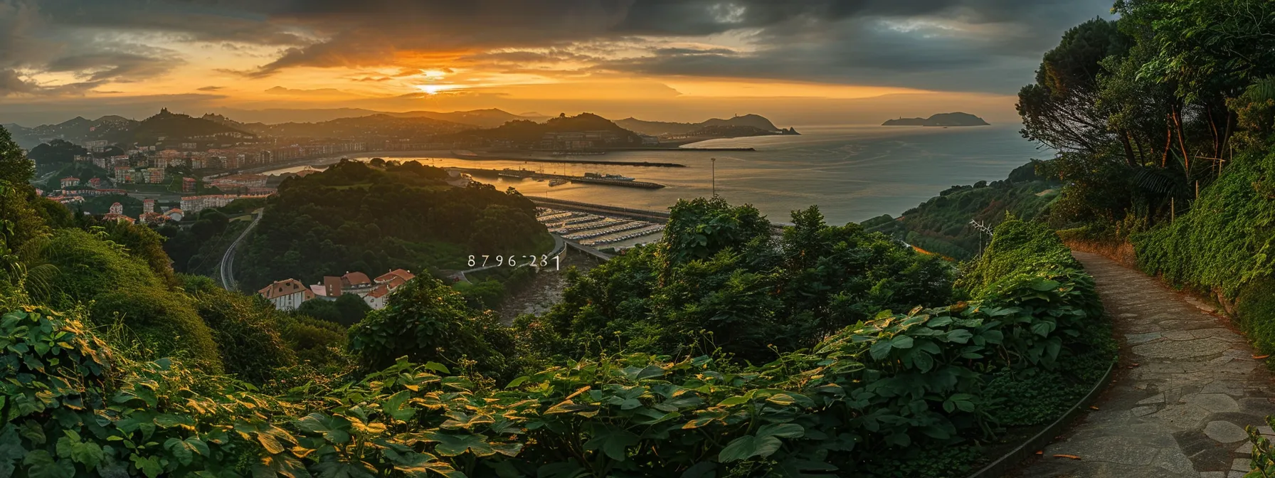 un sendero serpenteante en el monte ulia, rodeado de exuberante vegetación y ofreciendo vistas panorámicas deslumbrantes del puerto de san sebastián bajo la luz dorada del atardecer.