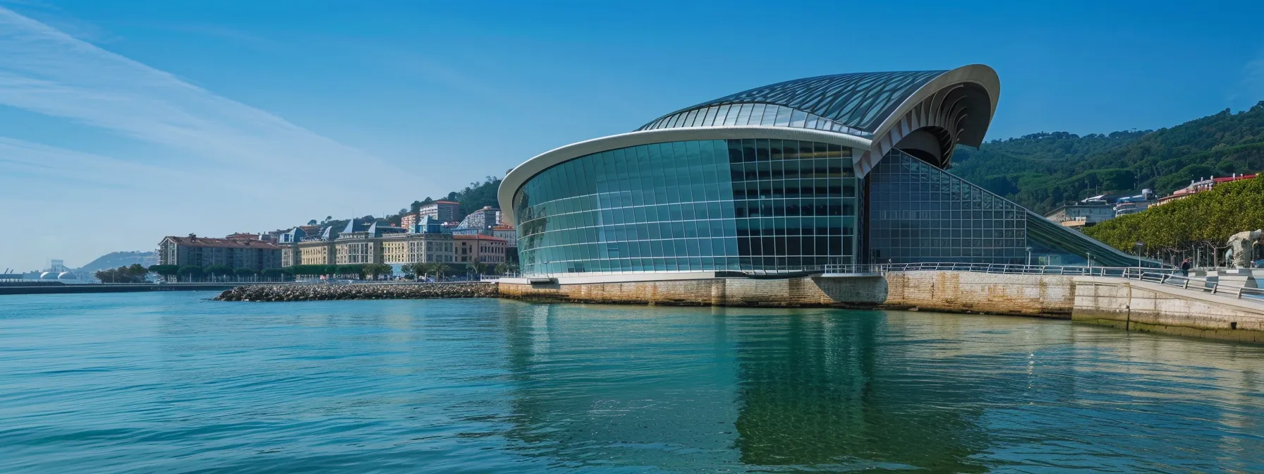 el palacio de congresos y auditorio kursaal se erige majestuosamente frente al mar, con su arquitectura moderna en contraste con la naturaleza circundante, bajo un cielo claro y luminoso que resalta su importancia cultural en san sebastián.